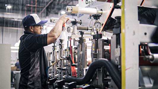 Photo of a man working with a machine that is converting bulk package adhesives into smaller packaging options.