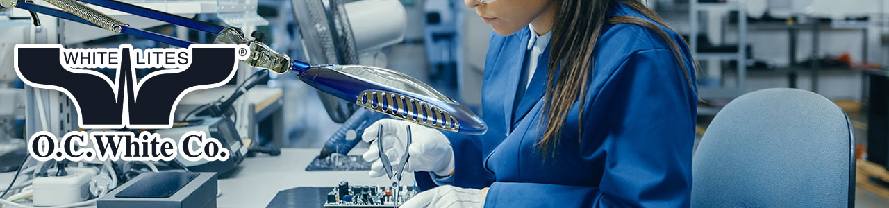A photo of a woman working on a motherboard while looking through an illuminated magnifier.